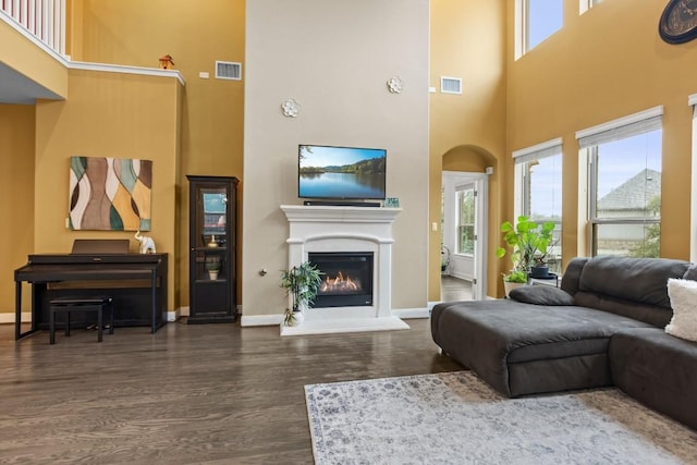 living room with a glass covered fireplace, visible vents, baseboards, and wood finished floors