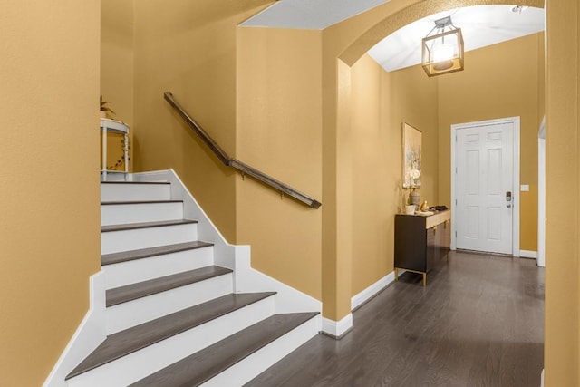 interior space featuring arched walkways, stairway, baseboards, and wood finished floors