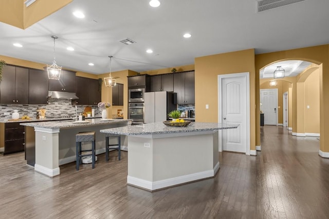 kitchen featuring arched walkways, visible vents, a kitchen island with sink, and stainless steel appliances