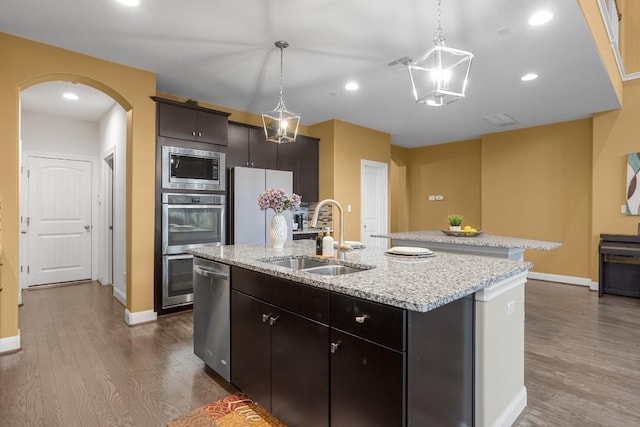 kitchen featuring visible vents, a center island with sink, dark wood finished floors, a sink, and appliances with stainless steel finishes