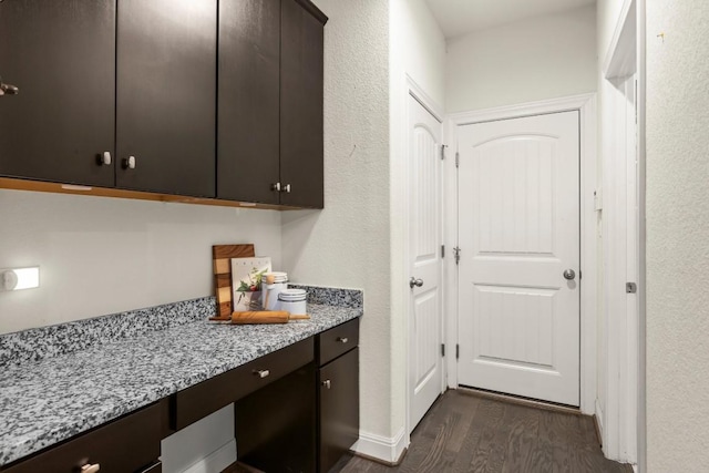 kitchen featuring dark wood-type flooring, light stone counters, dark brown cabinets, and built in study area