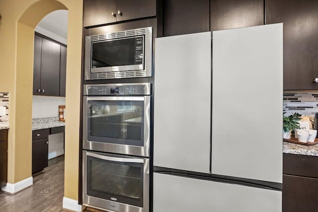 kitchen featuring light stone counters, wood finished floors, dark brown cabinetry, appliances with stainless steel finishes, and tasteful backsplash