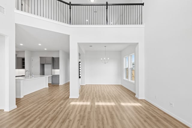 4419 College Square Dr, Round Rock, TX 78665 - unfurnished living room with visible vents, baseboards, a high ceiling, light wood-type flooring, and a notable chandelier