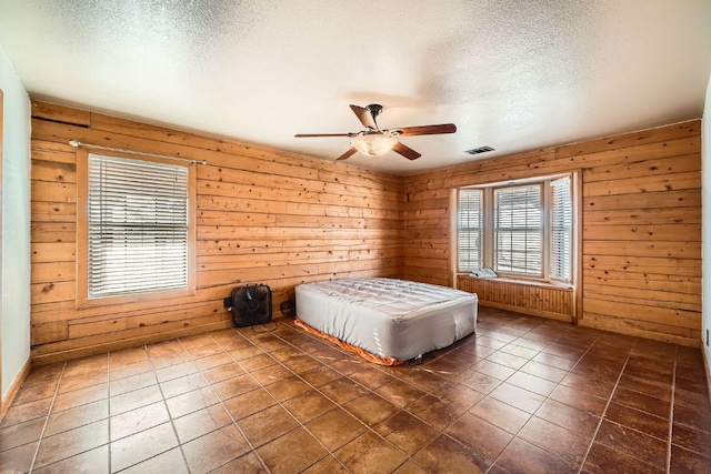 unfurnished bedroom with wooden walls, visible vents, dark tile patterned floors, a textured ceiling, and a ceiling fan