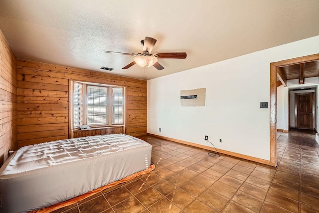 unfurnished bedroom with a ceiling fan, baseboards, visible vents, wood walls, and a textured ceiling