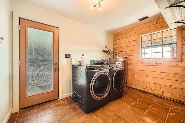 clothes washing area featuring tile patterned floors, visible vents, independent washer and dryer, wooden walls, and laundry area