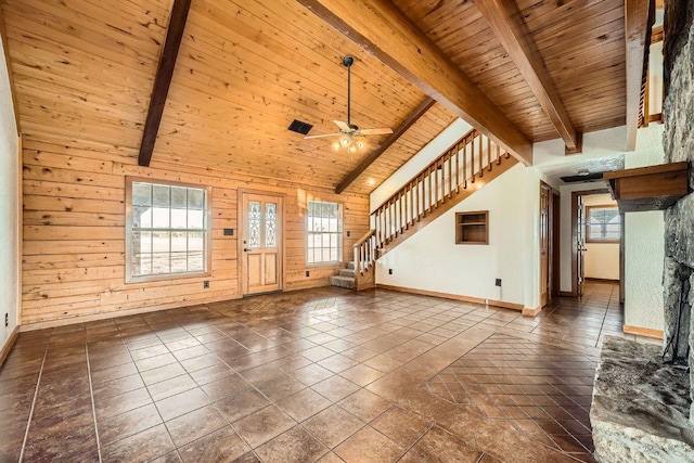 unfurnished living room with wooden walls, stairway, lofted ceiling with beams, a stone fireplace, and wooden ceiling