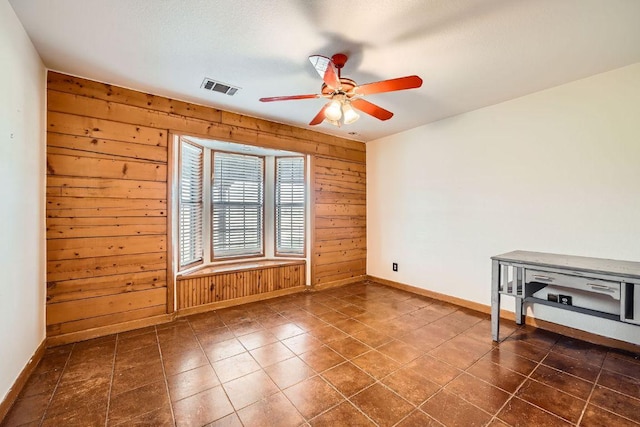 spare room featuring wooden walls, baseboards, visible vents, dark tile patterned flooring, and ceiling fan