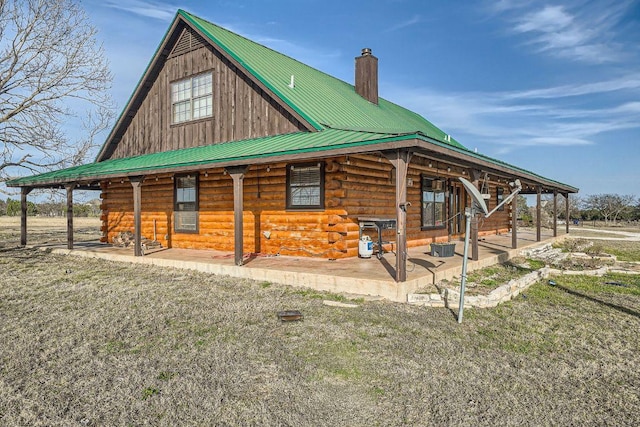 rear view of house featuring log siding, metal roof, and a chimney