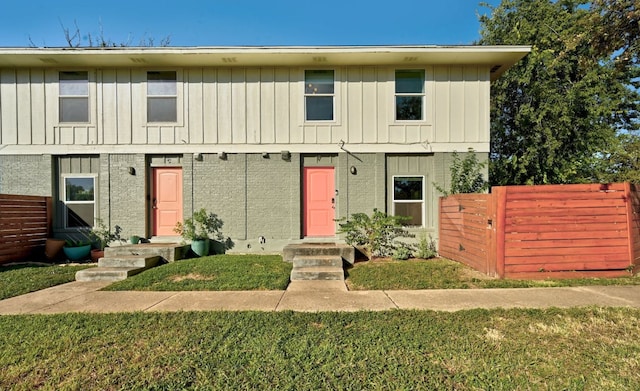 townhome / multi-family property featuring board and batten siding, a front lawn, and fence