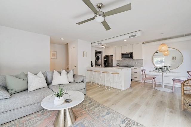 living area featuring visible vents, ceiling fan, stairs, stacked washer and clothes dryer, and light wood-type flooring