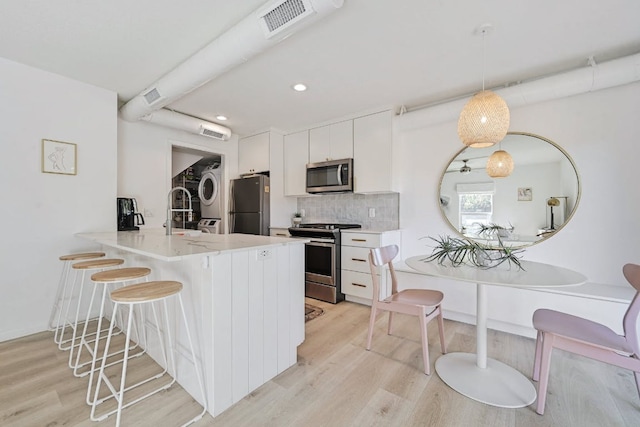 kitchen featuring light wood-style flooring, stacked washer and clothes dryer, appliances with stainless steel finishes, a kitchen breakfast bar, and tasteful backsplash