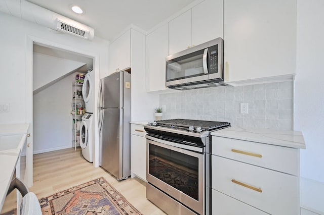 kitchen with visible vents, decorative backsplash, appliances with stainless steel finishes, white cabinetry, and stacked washer / dryer