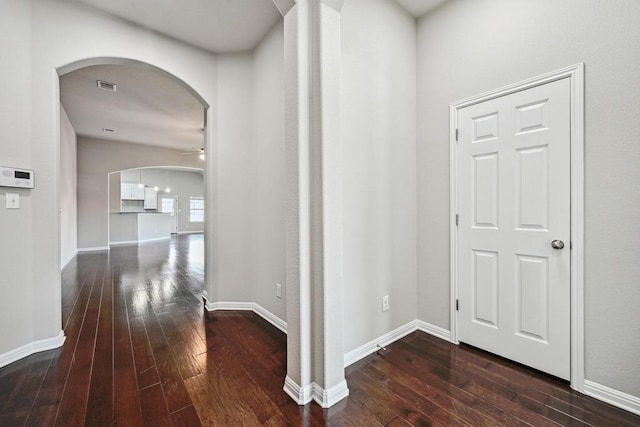 hallway featuring visible vents, arched walkways, baseboards, and dark wood-style flooring