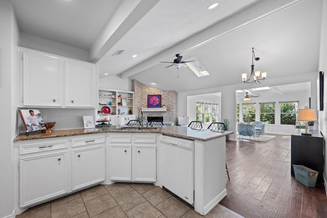 kitchen featuring open floor plan, vaulted ceiling with skylight, a peninsula, white dishwasher, and a sink