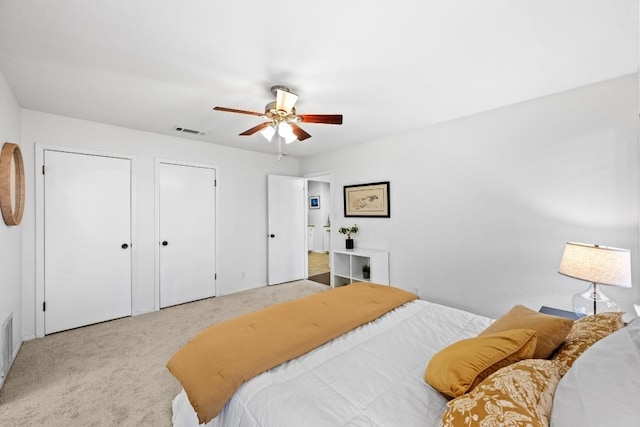 bedroom with two closets, visible vents, carpet floors, and ceiling fan