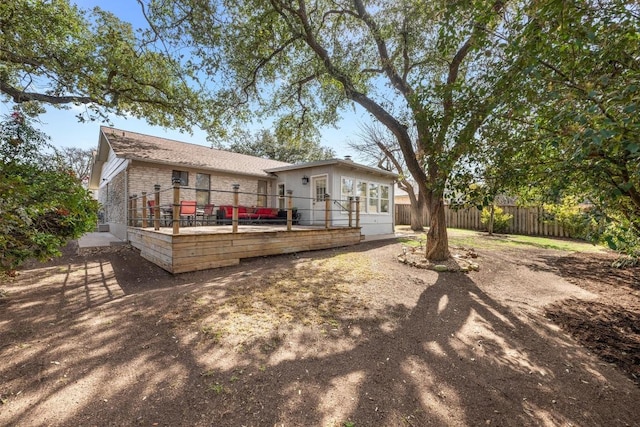 rear view of house featuring brick siding, a deck, and fence