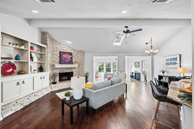 living room featuring visible vents, dark wood-type flooring, ceiling fan with notable chandelier, vaulted ceiling with skylight, and a fireplace