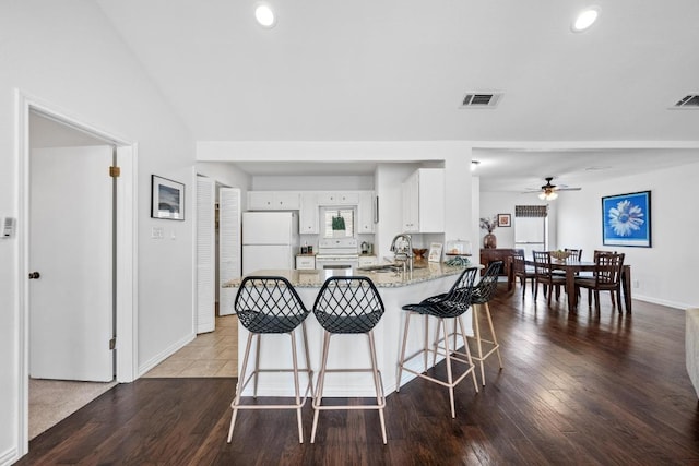 kitchen featuring visible vents, dark wood-type flooring, a sink, white appliances, and a peninsula