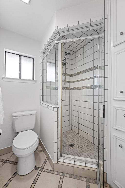 bathroom with tile patterned flooring, a shower stall, toilet, and baseboards