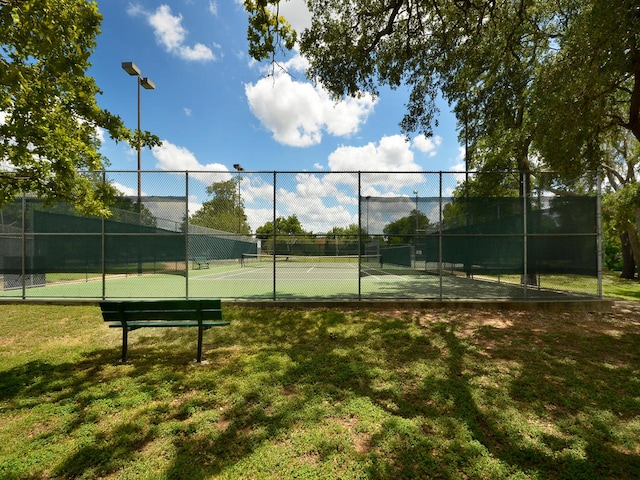 view of tennis court featuring a lawn and fence