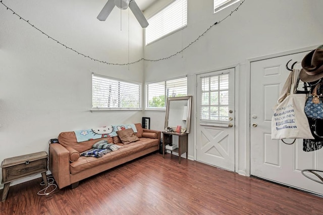 living room with ceiling fan, wood finished floors, and a towering ceiling