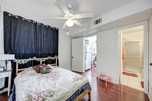 bedroom featuring visible vents, ensuite bathroom, freestanding refrigerator, wood finished floors, and a ceiling fan