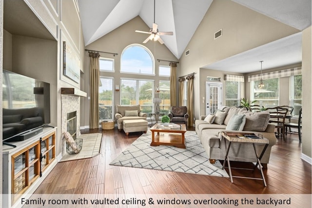 living area with visible vents, high vaulted ceiling, a stone fireplace, and hardwood / wood-style flooring