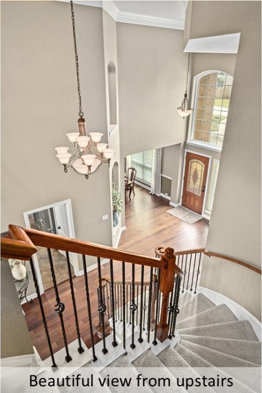 stairs with crown molding, baseboards, a chandelier, a high ceiling, and wood finished floors