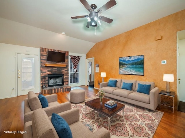 living room featuring lofted ceiling, a brick fireplace, wood finished floors, and a ceiling fan