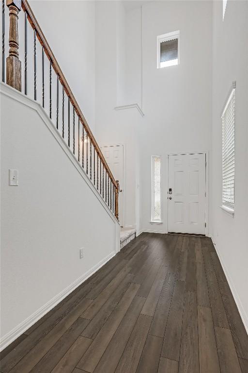 foyer entrance featuring dark wood finished floors, stairway, baseboards, and a towering ceiling