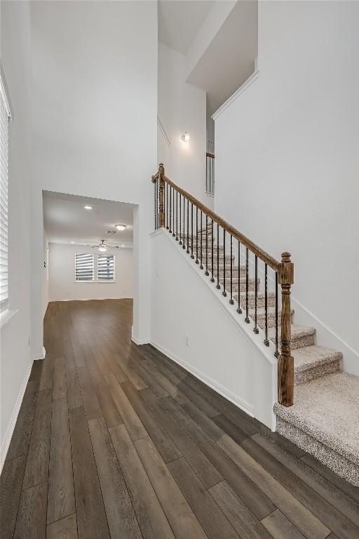 staircase with a ceiling fan, a high ceiling, baseboards, and wood finished floors