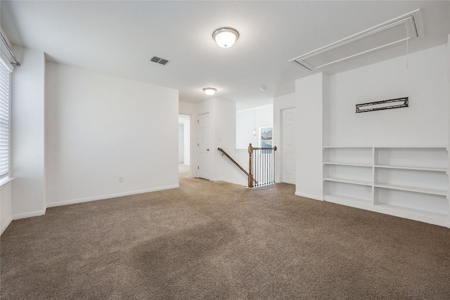 carpeted spare room with visible vents, attic access, and baseboards