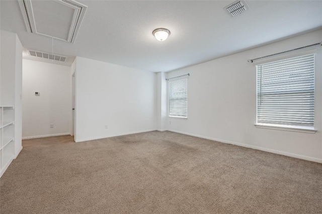 carpeted empty room featuring visible vents, attic access, and baseboards