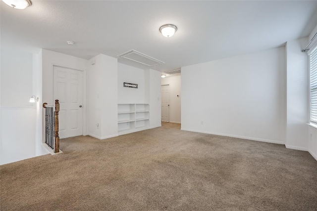 carpeted empty room with attic access, built in features, and baseboards