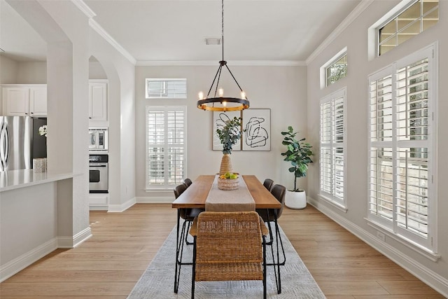 dining space with visible vents, baseboards, arched walkways, ornamental molding, and light wood-type flooring