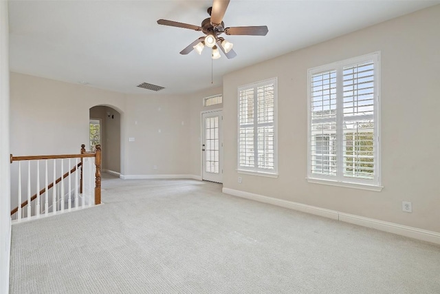 carpeted spare room featuring arched walkways, plenty of natural light, visible vents, and baseboards