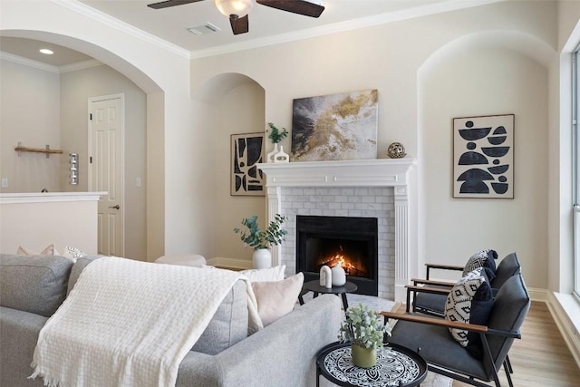 interior space with wood finished floors, visible vents, a fireplace, ceiling fan, and ornamental molding