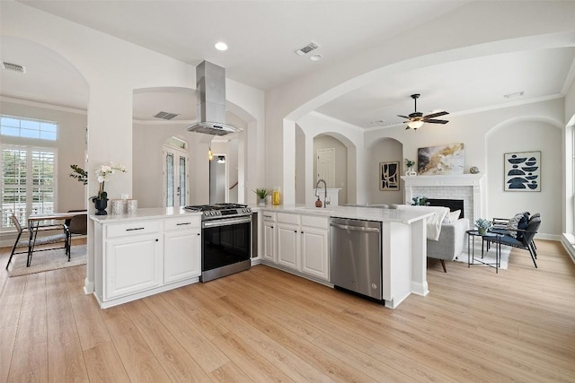 kitchen featuring visible vents, a brick fireplace, appliances with stainless steel finishes, a peninsula, and wall chimney exhaust hood