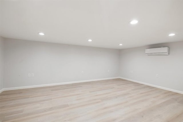 finished below grade area with a wall mounted air conditioner, baseboards, light wood-style floors, and recessed lighting