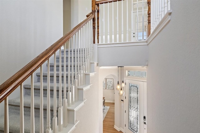 stairway featuring wood finished floors, arched walkways, and a towering ceiling