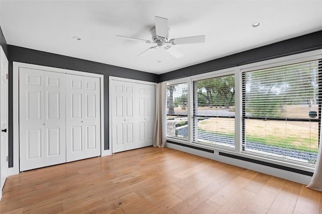 unfurnished bedroom featuring two closets, wood finished floors, a ceiling fan, and recessed lighting