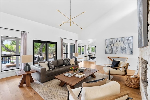 living area with a towering ceiling, light wood-type flooring, a wealth of natural light, and a chandelier