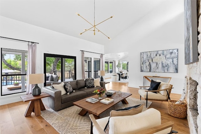living room with healthy amount of natural light, high vaulted ceiling, light wood finished floors, a chandelier, and baseboards