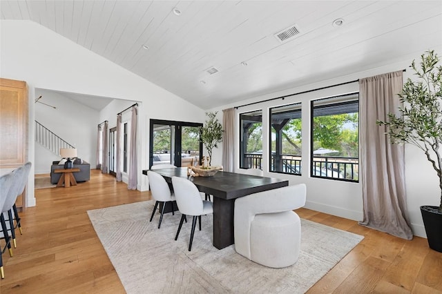 dining space with healthy amount of natural light, stairs, light wood-type flooring, french doors, and high vaulted ceiling