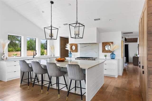 kitchen with light wood finished floors, a kitchen island, a breakfast bar area, white cabinetry, and decorative light fixtures