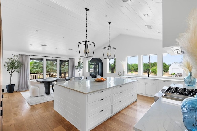 kitchen with white cabinetry, vaulted ceiling, light stone countertops, a kitchen island, and light wood-type flooring