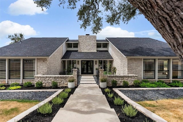 exterior space with a shingled roof, french doors, stone siding, and a chimney