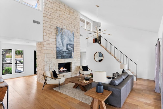 living area featuring a towering ceiling, a stone fireplace, light wood-type flooring, stairway, and baseboards
