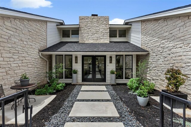 entrance to property with french doors, a chimney, and a shingled roof